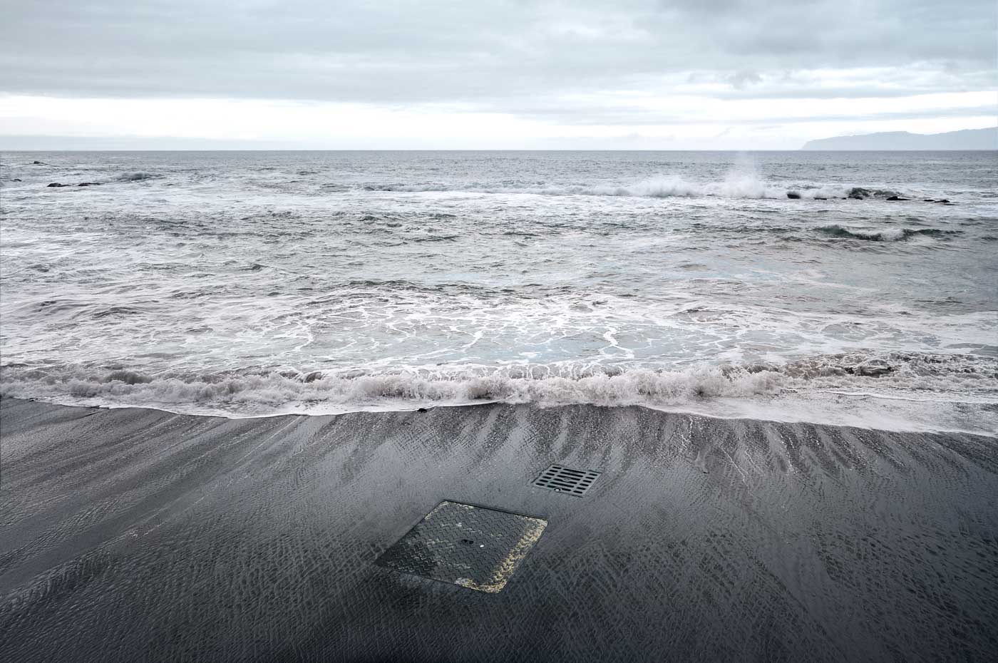 imaginary manhole cover on a black sandy beach